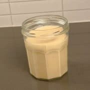 A glass jar with no lid containing mayonnaise sitting on a grey benchtop.