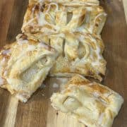 Rectangles of golden-brown puff pastry with poached pear inside displayed on a wooden chopping board.
